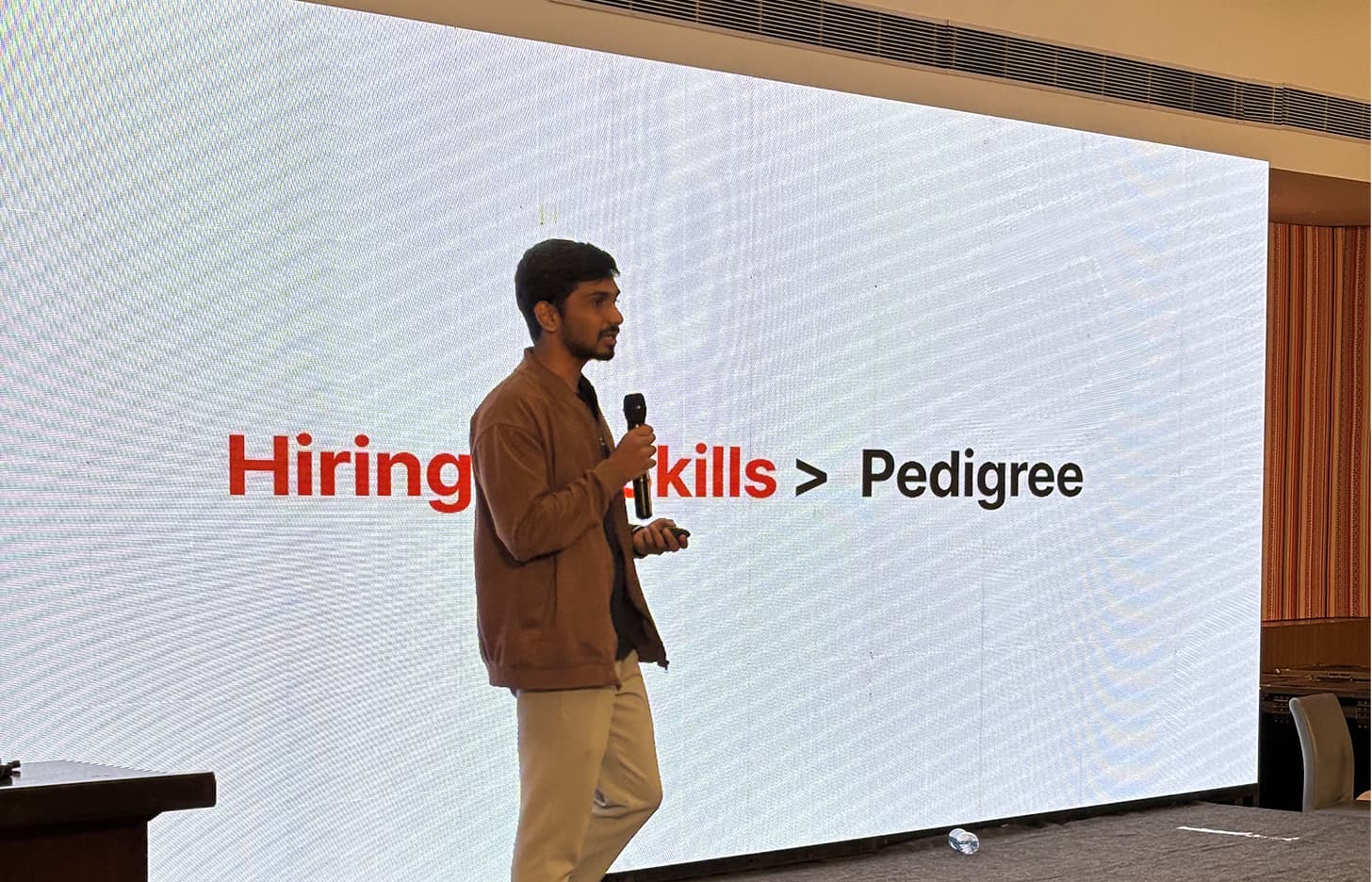 Record speaker on stage presenting "Hiring: Skills > Pedigree"